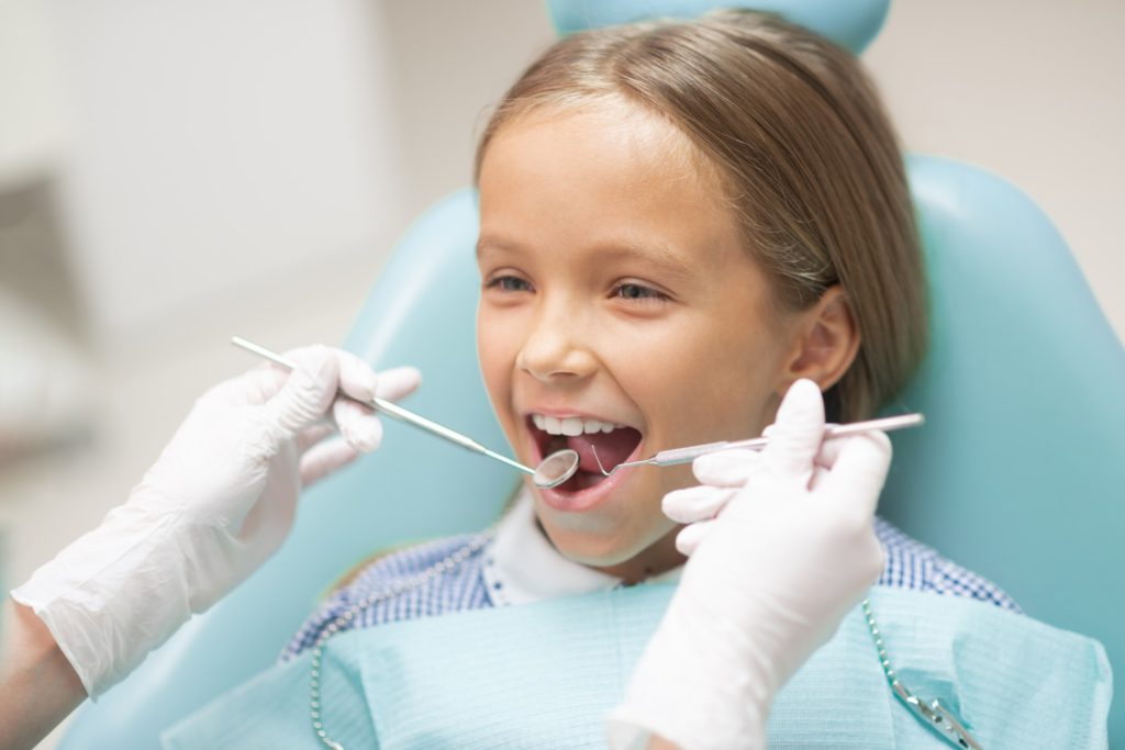 A young girl sits in a dental exam chair receiving a dental checkup