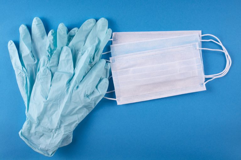 A pair of surgical gloves and medical masks laying on a blue background
